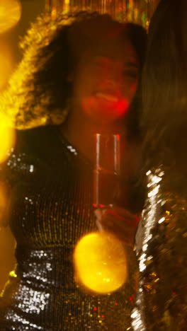 Vertikales-Video-Von-Zwei-Frauen-In-Einem-Nachtclub-Oder-Einer-Bar,-Die-Tanzen-Und-Alkohol-Trinken,-Mit-Funkelnden-Lichtern-Im-Hintergrund